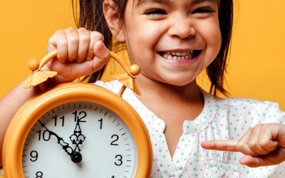 Smiling little girl child holding clock alarm. Photo of smiling little girl child standing isolated over yellow background. Looking camera holding clock alarm.